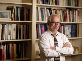 a middle aged white man standing in front of a bookcase smiling