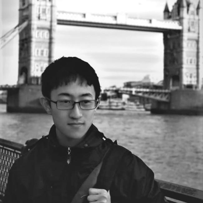 a young Asian male standing in front of a bridge along a river