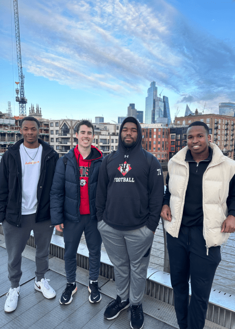 a group of four young men standing in front of a city skyline