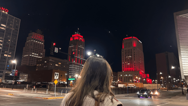 a young woman stands in front of a red skyline in a small city