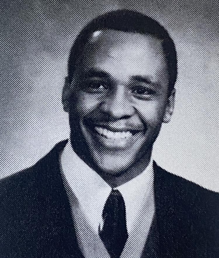 a black and white photo of a young man wearing a suit and tie smiling