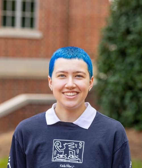 A young person with blue hair wearing a sweatshirt and collar smiles