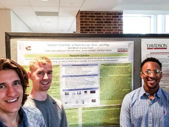 Three students stand around their research posters, ready to present