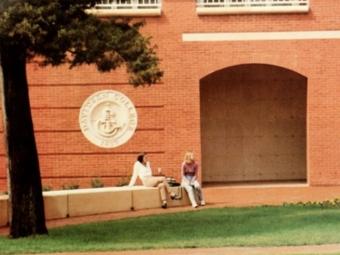 two students sit on a wall outside of a brick building