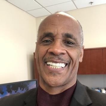 a middle aged Black man smiling while wearing a suit and tie