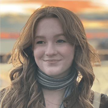 a young white woman with curly brown hair wearing a scarf in front of a sunset
