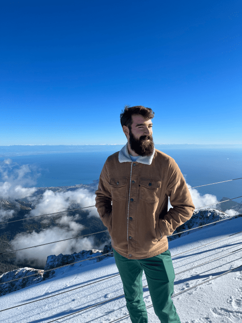 a young man stands on a snowy mountain top with a blue sea in the background