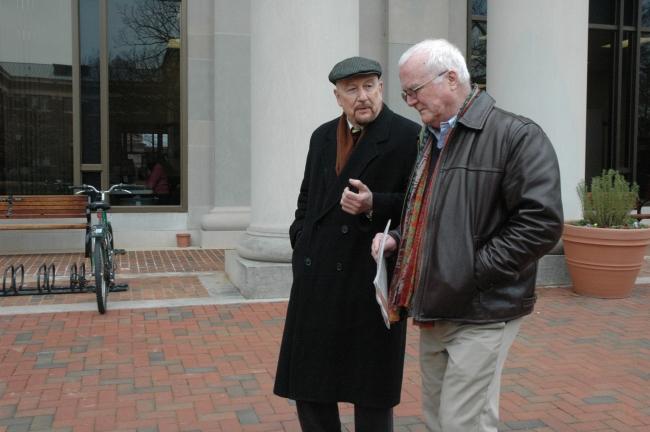 two older white men walk in front of a library while talking to each other