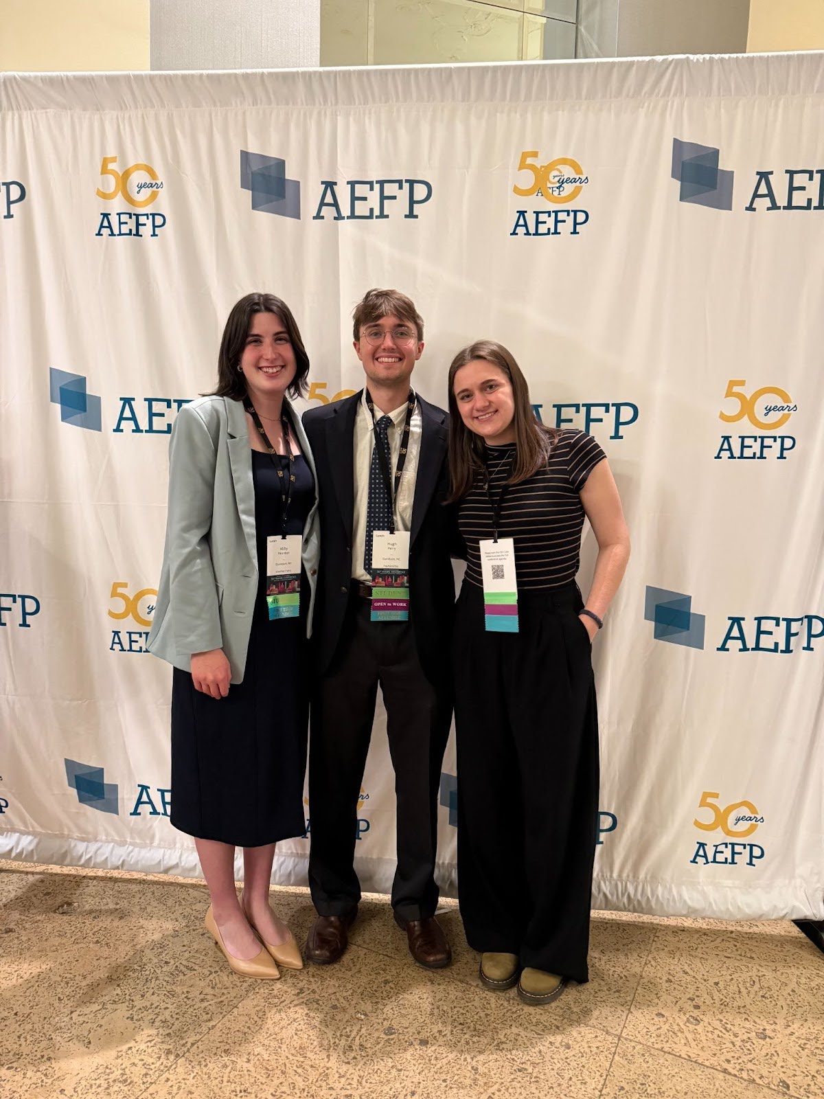 a group of three students in business casual smile together at a conference