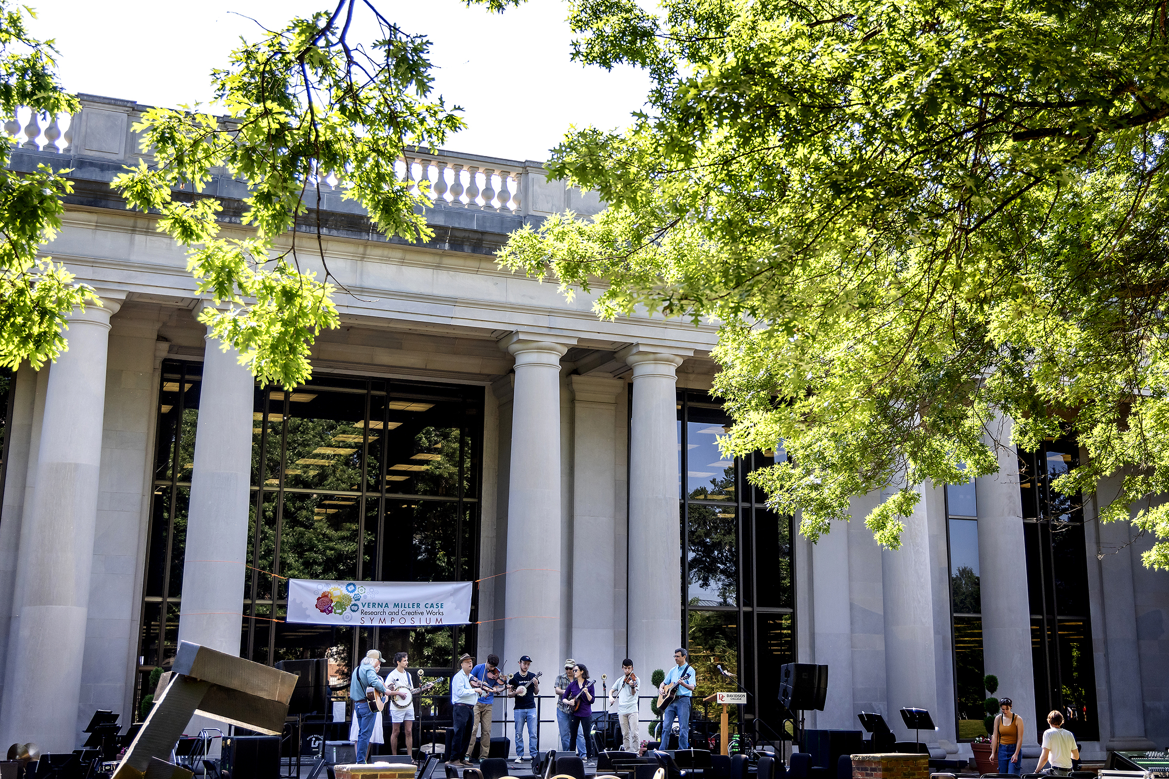 a group of students perform music in front of a columned academic building on a sunny day
