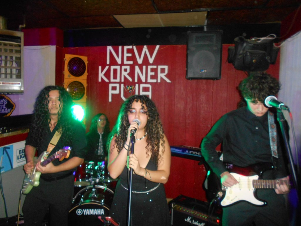 A group of students stand on a dimly lit stage with instruments