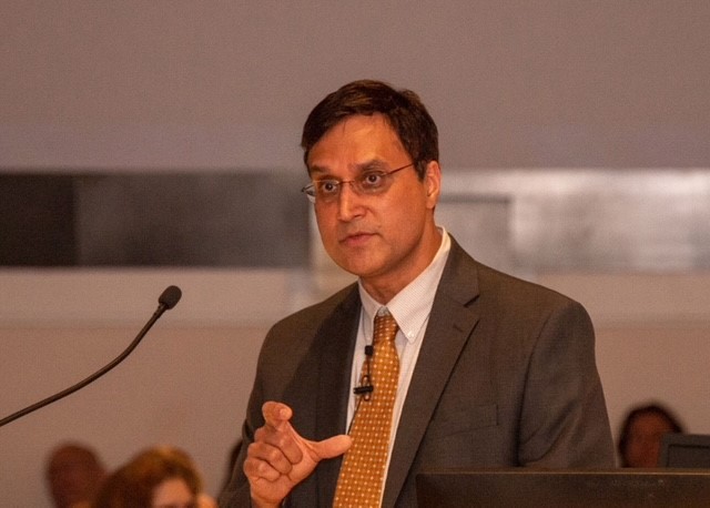 a man wearing a suit and tie speaks into a microphone on stage