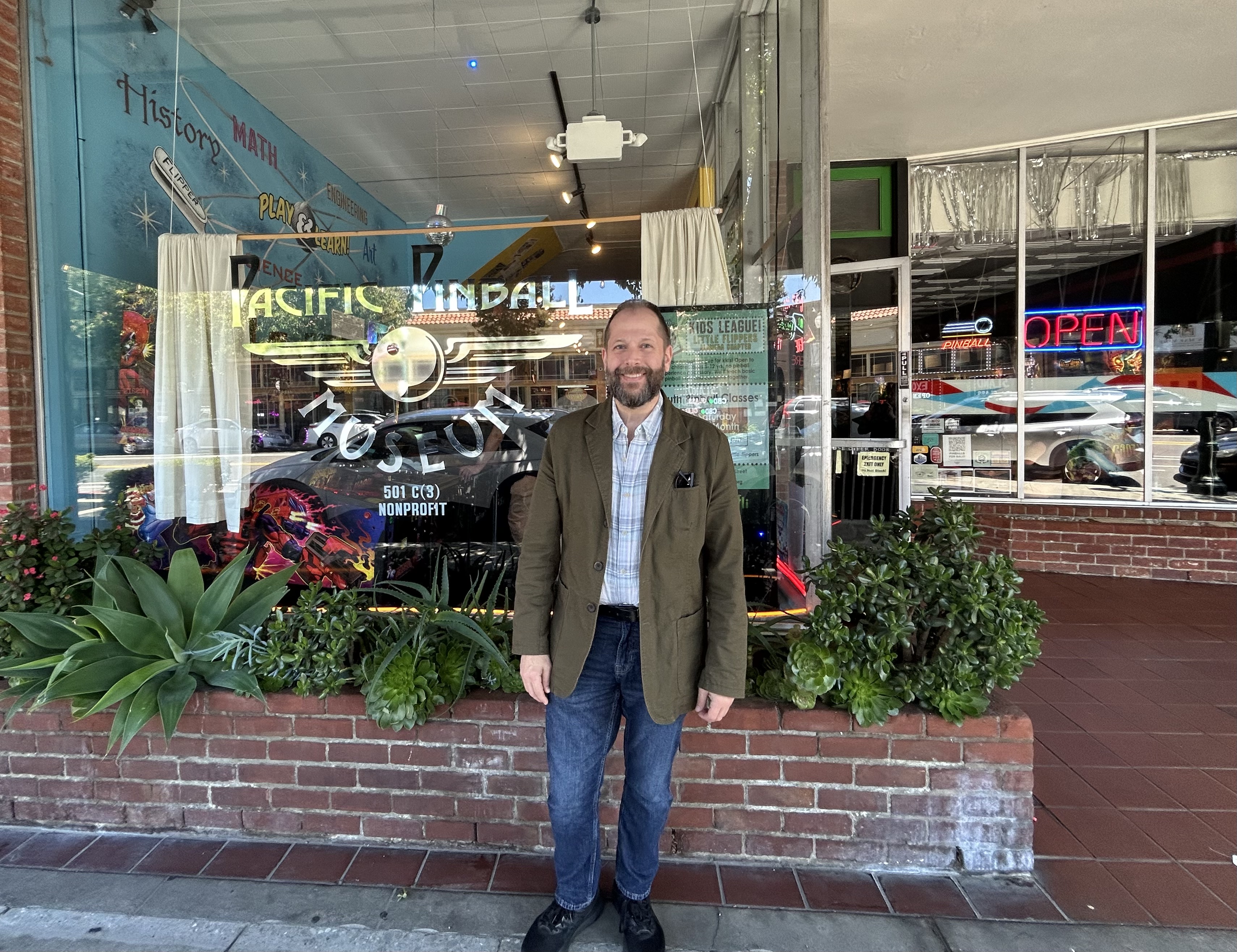 a man stands in front of a pinball museum smiling
