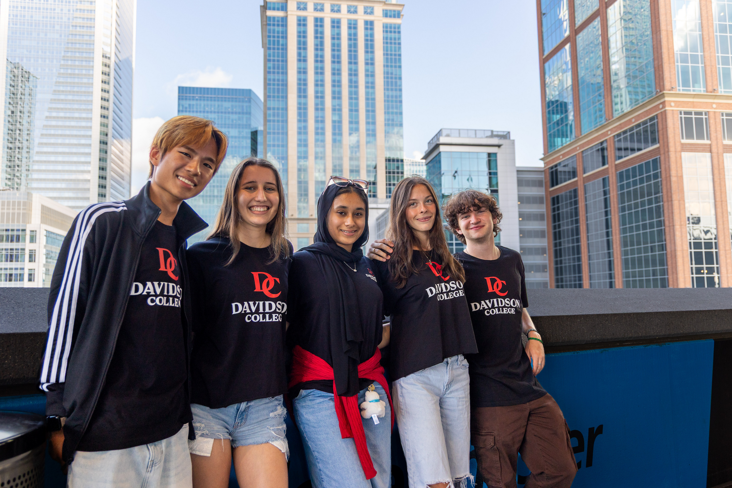 Five students in black and red Davidosn College shirts, with skyscrapers in the background
