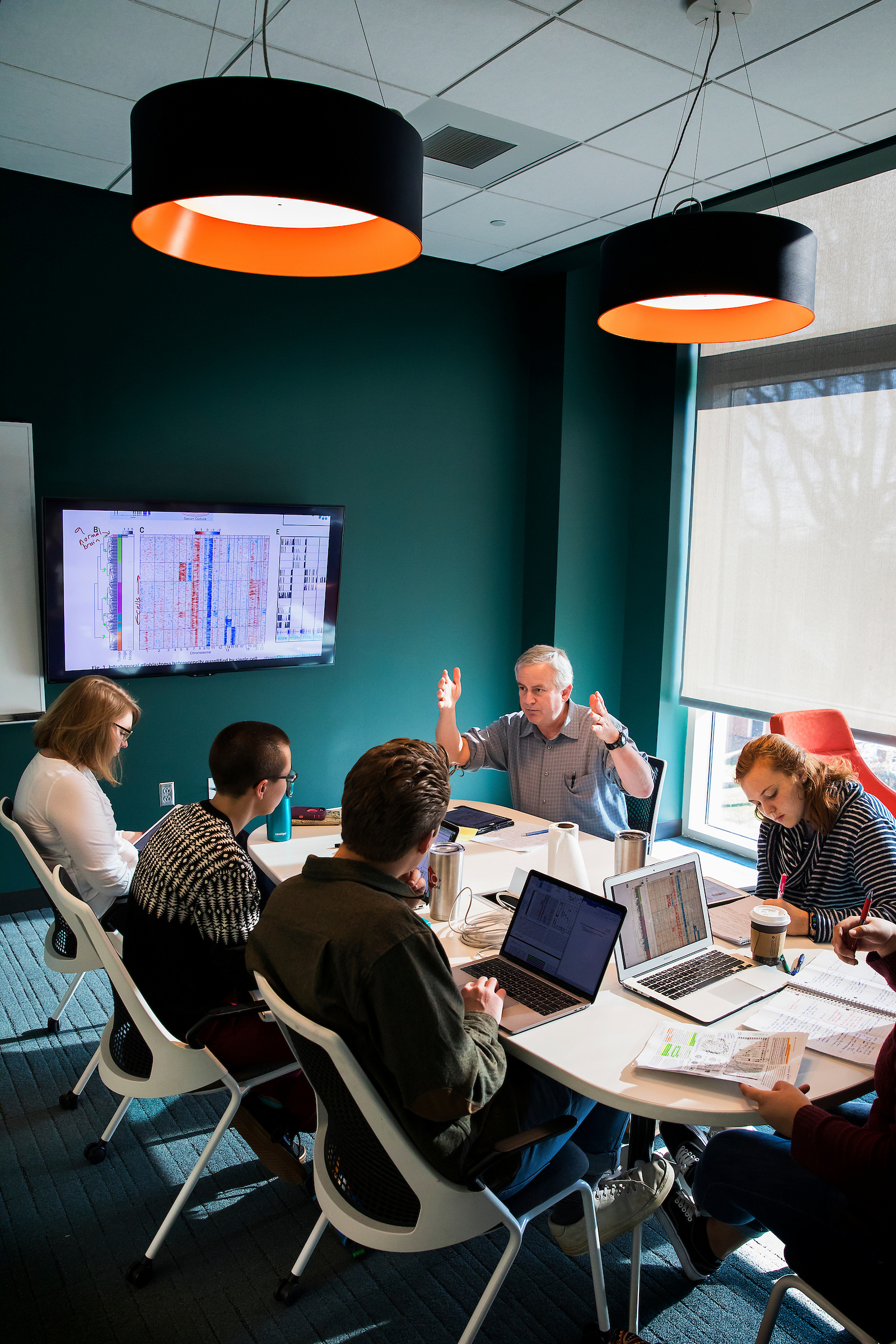 A professor leads a discussion with students gathered around a seminar table in a campus classroom