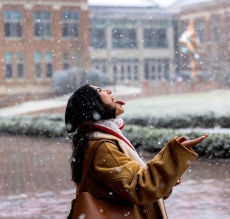 a young woman holds out her tongue to catch a snowflake on a college campus covered with snow