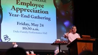 an older man speaks into a podium in front of a screen that reads "Employee Appreciation Year-End Gathering"