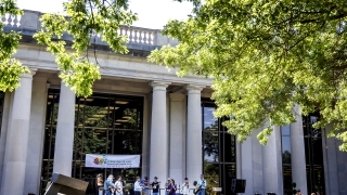 a group of students perform music in front of a columned academic building on a sunny day