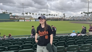 a young woman wearing an Orioles baseball jersey and hat in front of a baseball stadium