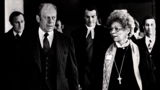 a Black woman walks and talks with an older white man in a black and white photograph
