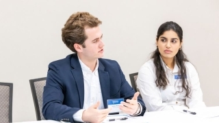 two students discuss at a roundtable while wearing business attire