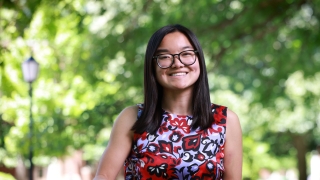 A smiling student with glasses and straight, dark hair poses outside wearing a sleeveless floral patterned blouse.