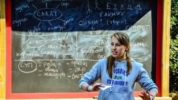 Russian studies TA stands in front of outdoor chalkboard showing writing in Russian