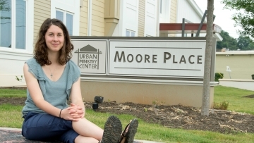 Elizabeth Welliver '16 sits on pavement next to the Moore Place community organization sign