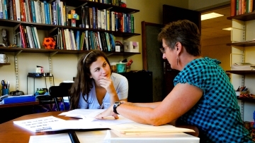 Prof. Molinek sits in her office with student looking at printed materials