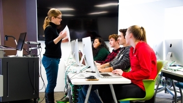 Prof. Peck talks to four students that each use a desktop computer