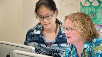 Prof. Heyer and a student look at data on a desktop computer in a lab