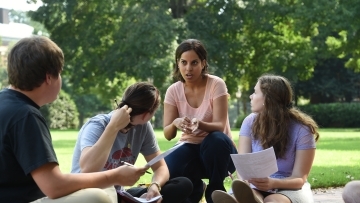 Professor kneals with students while leading class outside