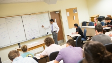 Economics professor writes on board while students take notes
