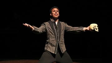 Performer on his knees sings a song while holding a skull