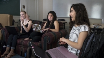 Three students smiling and talking to each other on a couch