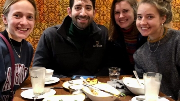 three young women and a young man smile while sitting around a restaurant table together