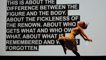 a dancer moves in front of a screen with a block of text on it
