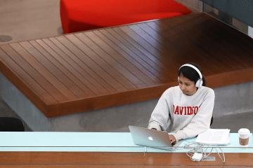 student wearing a Davidson sweatshirt and headphones works on a laptop in a modern academic building