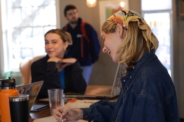 two students smile while working in a coffee shop