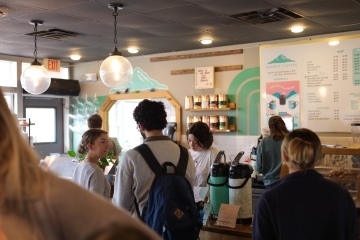 a group of students smile and talk while waiting in line at a coffee shop