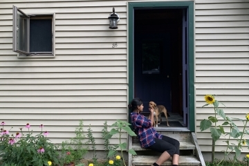 a young woman sits on a staircase outside of a house with a dog surrounded by flowers