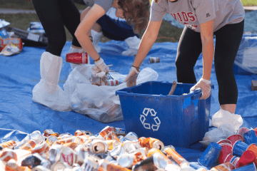 two young people holding recycling bins while sorting through piles of trash