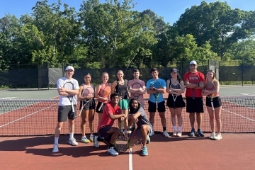 a group of students with tennis rackets on a court smiling