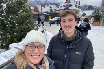 an older white woman and a younger white man smile in front of a snowy landscape