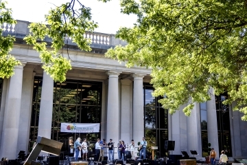 a group of students perform music in front of a columned academic building on a sunny day