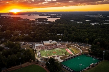an aerial view of a football stadium as the sun sets in the distance over a lake