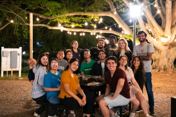 a group of young people sitting together at night with string lights in the background