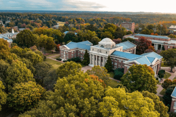 an aerial view of a college campus with brick buildings, green trees and a lake in the distance