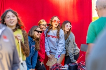 a group of young women and their moms pose in front of a red photo booth
