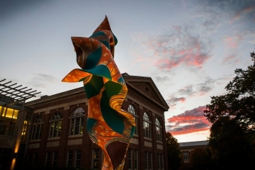 a colorful sculpture in front of an academic building at sunset